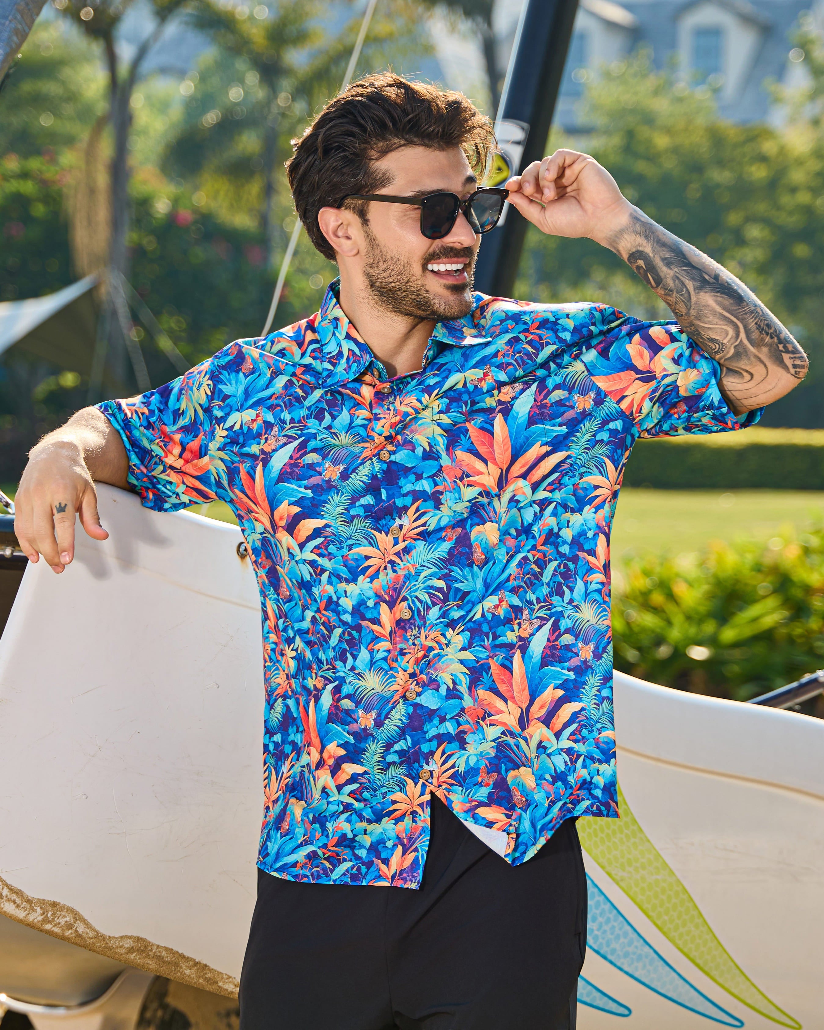 Man in a colorful shirt standing next to a sailboat with trees and grass in the background