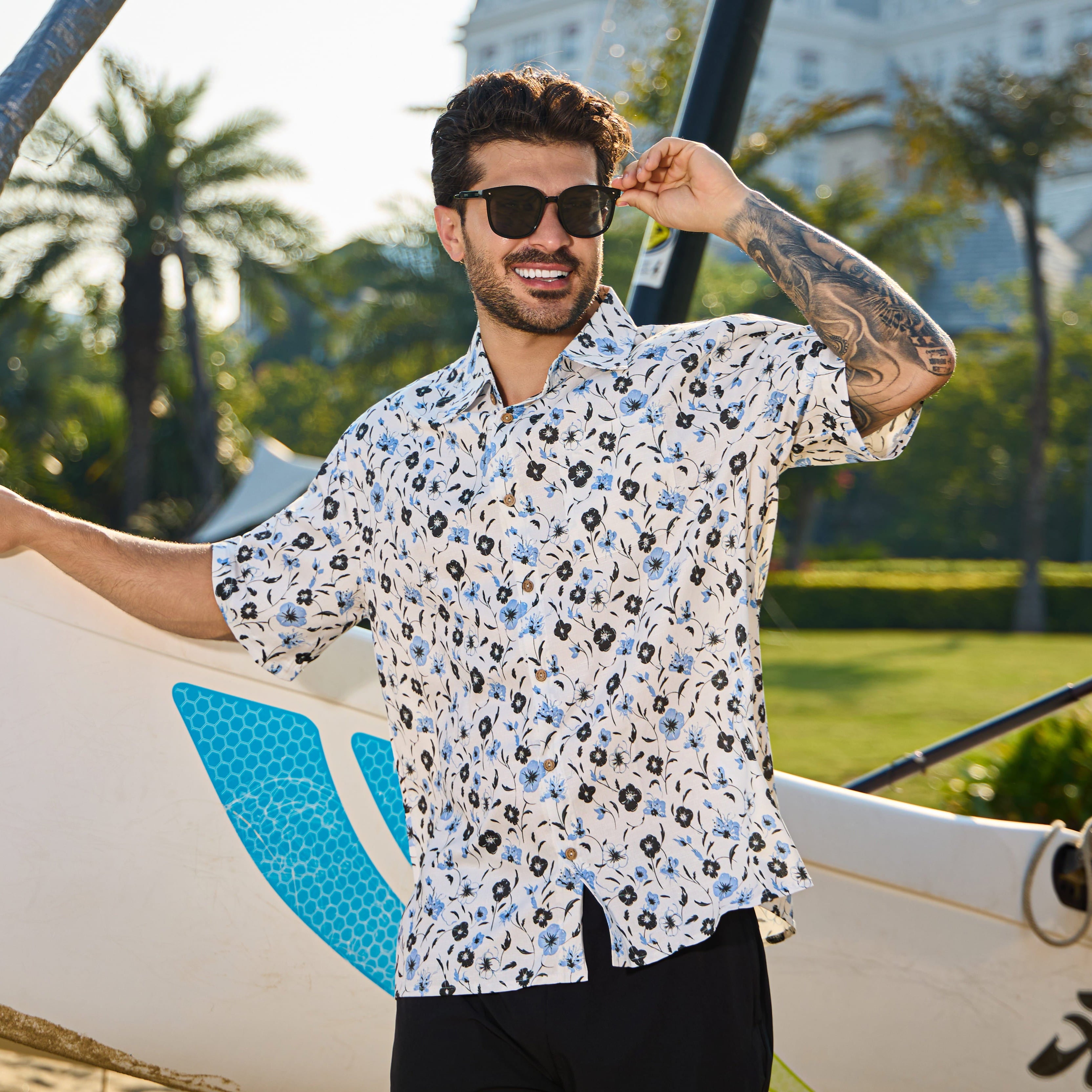 Man holding a surfboard with palm trees and a building in the background