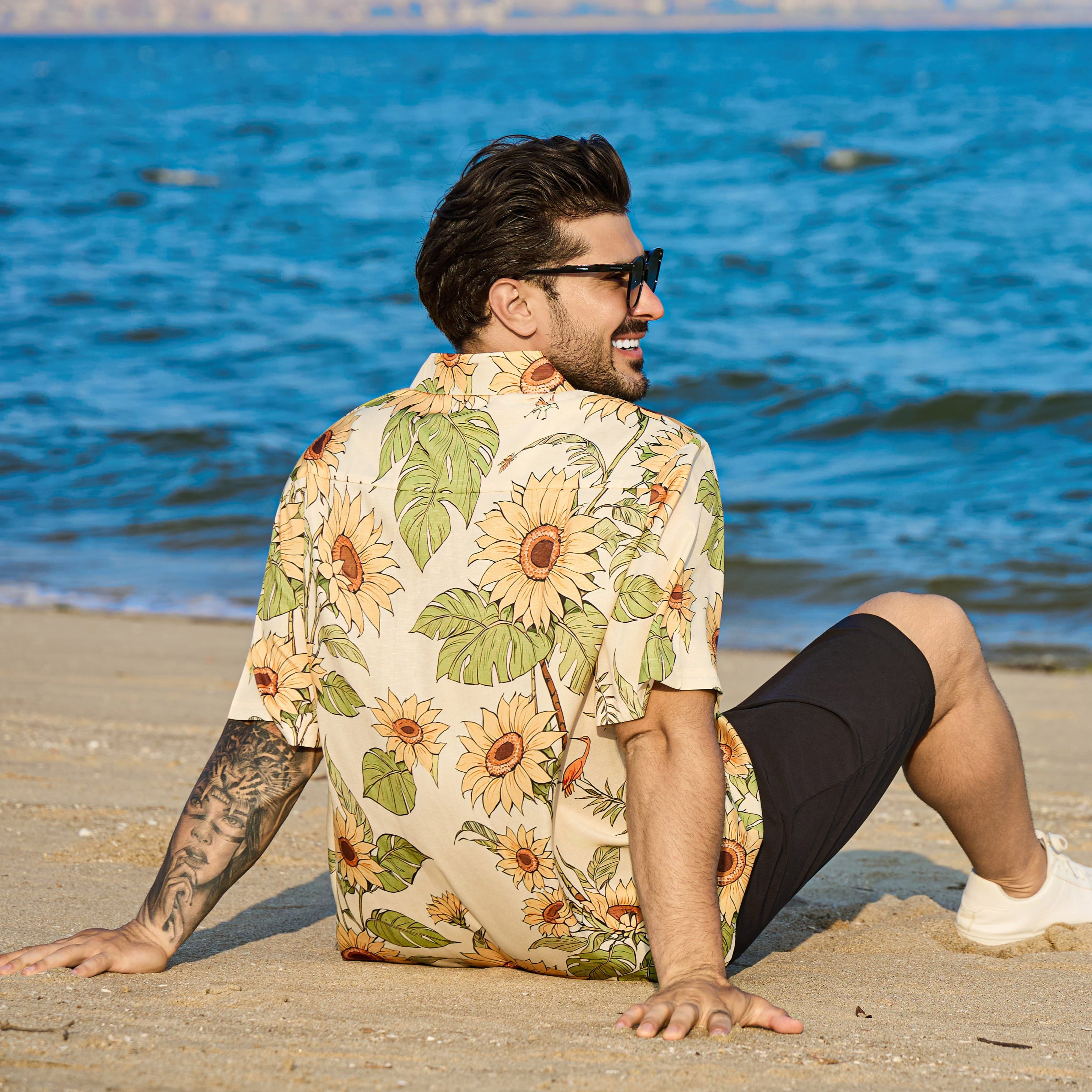 Man sitting on a beach wearing a floral shirt and sunglasses
