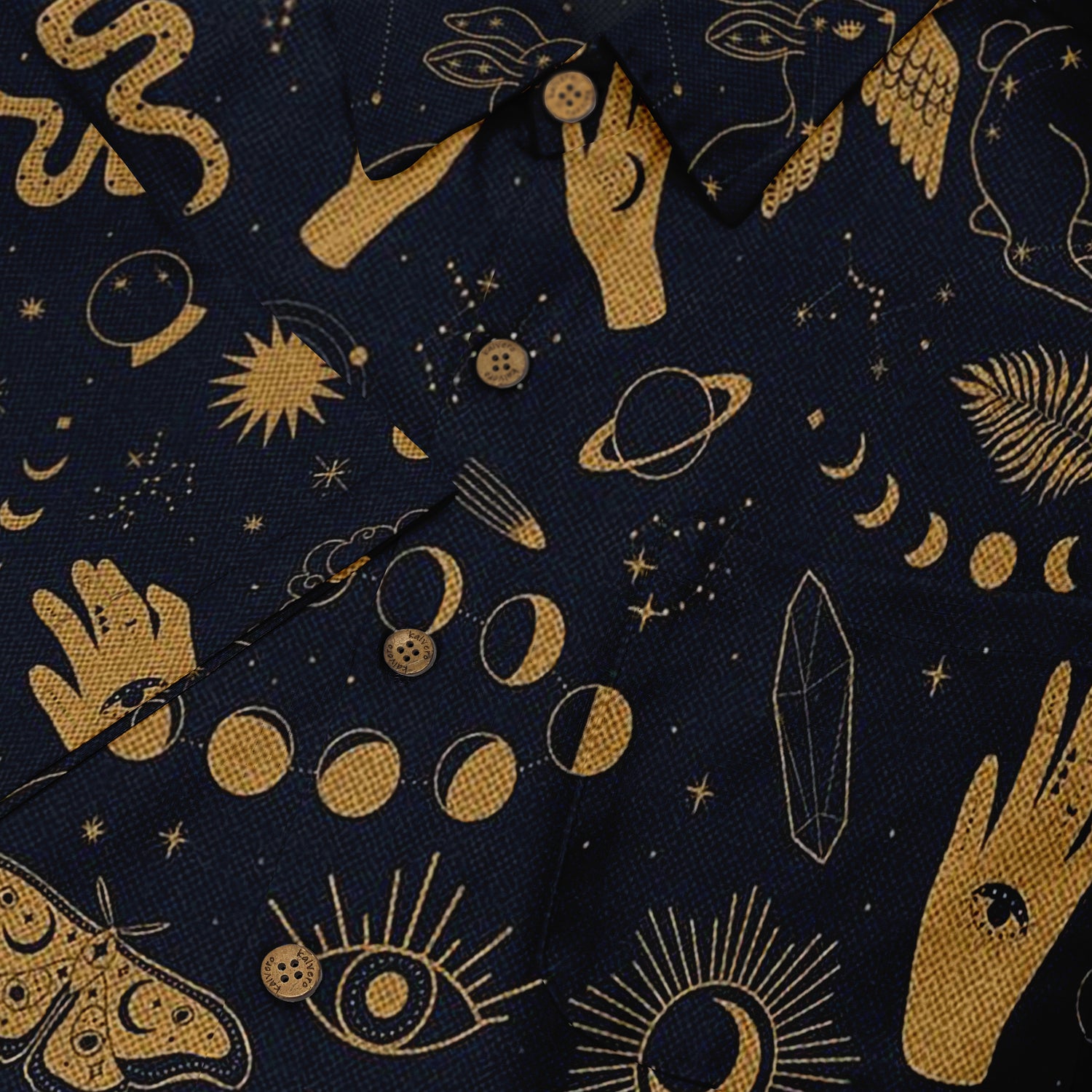 Close-up of a shirt featuring mystical gold illustrations on dark fabric, including hands, moons, suns, and other celestial symbols.