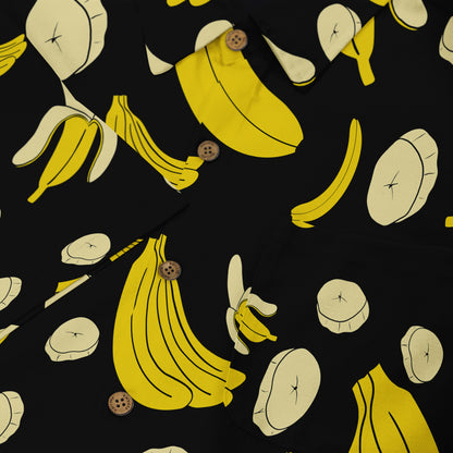 Close-up of a black shirt featuring a playful banana print with vibrant yellow and cream bananas, peeled bananas, and banana slices, accented with wooden buttons.