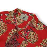 Close-up of a Hawaiian shirt collar with a bold red background, featuring large, multicolored leopard-print leaves and red accents. The Kalvero logo is visible on the inner tag.