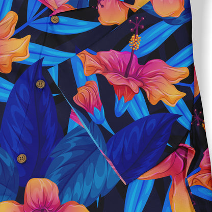 This image shows a close-up of a Hawaiian shirt with vibrant blue leaves and pink-orange flowers on a dark background, highlighting the detailed floral pattern.