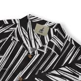 A close-up of a shirt collar featuring a bold white palm leaf pattern on a black background, with a "Kalvero" label visible.