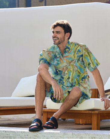 Man in colorful shirt and shorts, sitting on lounge chair.