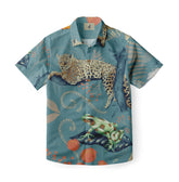 This is a shirt with a jungle-themed design, featuring a leopard, a monkey, a frog, and tropical plants against a soft teal background.