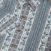 A short-sleeved shirt with a "Serenity Scrolls" pattern, featuring blue and white paisley motifs and floral vines framed by geometric borders front buttons close-up