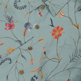 Close-up of a light green shirt with a detailed floral and botanical design, featuring colorful flowers, thin branches, and natural elements, complemented by wooden buttons.