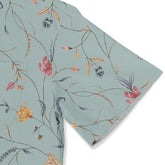 Close-up of a light green shirt sleeve with a delicate floral and botanical pattern, featuring thin branches and colorful flowers, adding a soft, elegant touch.