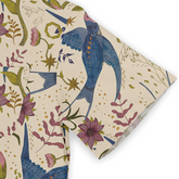 This is a close-up of a shirt sleeve featuring a whimsical design with vibrant blue birds and pink flowers, set against a light beige background. The pattern includes various floral elements and stars, enhancing the playful and artistic style of the shirt.