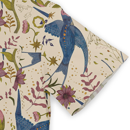 This is a close-up of a shirt sleeve featuring a whimsical design with vibrant blue birds and pink flowers, set against a light beige background. The pattern includes various floral elements and stars, enhancing the playful and artistic style of the shirt.