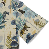 This is a close-up of a shirt sleeve featuring a design with botanical elements and leopard motifs in shades of blue, green, and beige, set against a textured, earthy background. The sleeve showcases detailed leaves and leopard silhouettes, enhancing the nature-inspired theme of the shirt.